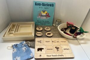 Educational display with a wooden puzzle board showing four food chiefs and text in multiple languages, plus wooden boxes and tokens for a language game.
