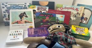 A collection of children's books and a plush puppet arranged on a table, including 'Sometimes I Feel Like a Fox' and Crayola Colors of the World.