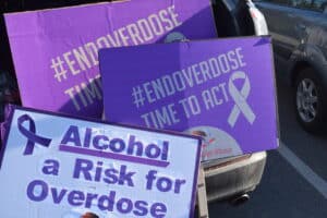 Purple protest signs with the hashtag #ENDOVERDOSE and the slogan 'Time to Act' leaning against a car in a parking lot.
