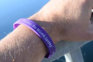 Close-up of a purple wristband on a hairy forearm, with partially visible white text in a bright outdoor setting.