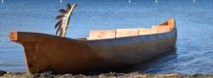 Wooden canoe at the water's edge on a calm lake, with rocky hills and blue sky in the distance.