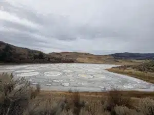 Overcast sky over a basin of circular salt ponds with distant brown hills on the horizon.