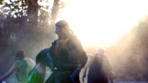 People wearing life jackets outdoors, standing in a sunlit, smoky scene as they participate in an activity.