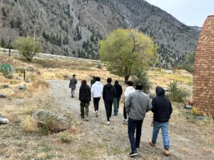 Group of people walking away on a gravel path through a dry field with steep rocky mountains in the background.